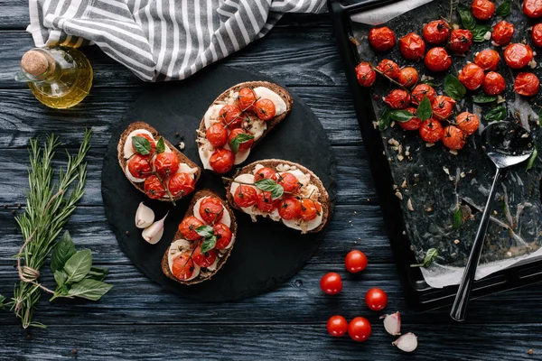 Вкусные бутерброды с моцареллой и запечёнными помидорами на темной доске — стоковое фото