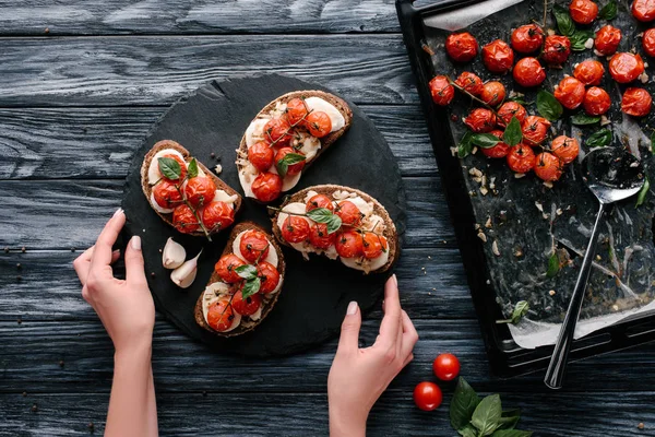 Mulher que serve sanduíches com queijo e tomates assados no tabuleiro de ardósia escura — Fotografia de Stock