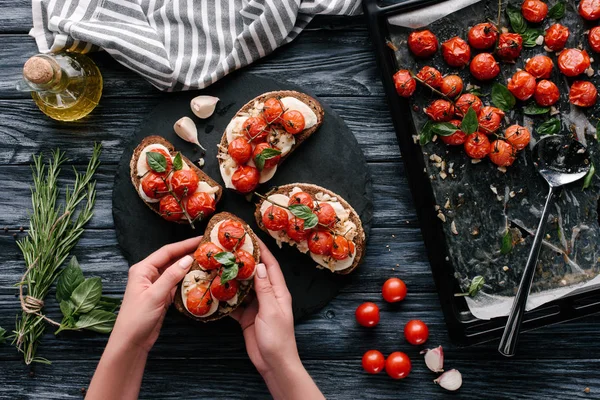 Cocinera femenina cocinando sándwiches con queso y tomates horneados sobre mesa de madera oscura - foto de stock