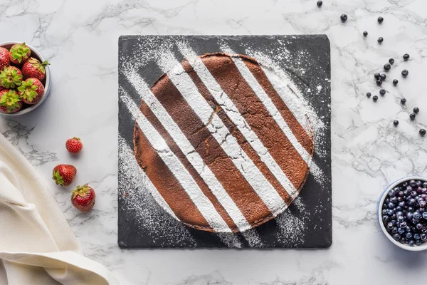 Vue de dessus de délicieux gâteau brun fait maison avec cerise sur panneau d'ardoise et baies fraîches sur la surface de marbre — Photo de stock