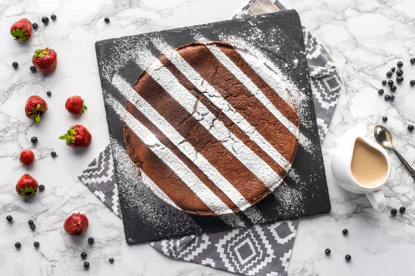 Вид на вкусный домашний коричневый торт с сахарным порошком и свежими ягодами на мраморной поверхности — стоковое фото