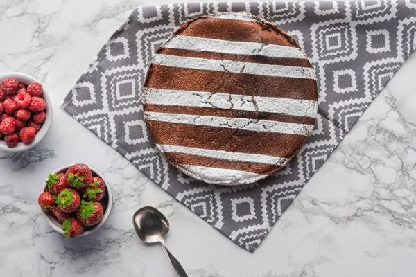 Вид на вкусный коричневый торт с сахарным порошком и свежими ягодами на мраморной поверхности — стоковое фото
