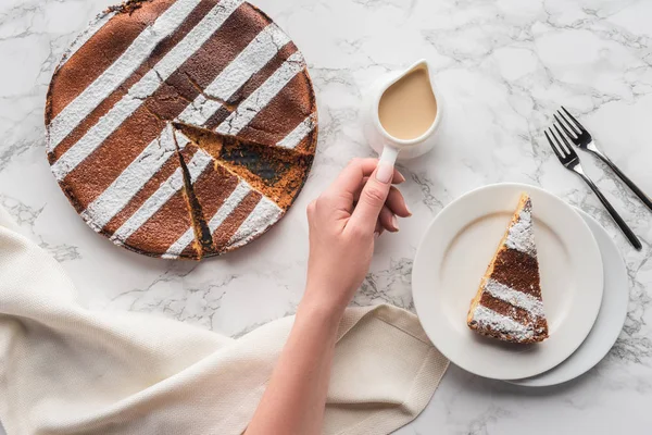 Cropped shot of person holding jug with hot chocolate and delicious homemade cake on marble surface — Stock Photo