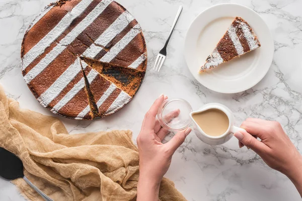 Cropped shot of person pouring hot chocolate above marble surface with delicious homemade cake — Stock Photo