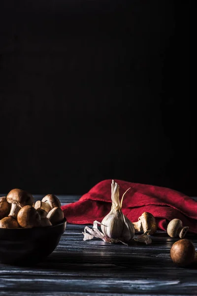 Selektiver Fokus der Schüssel mit Pilzen und Knoblauch auf Holztisch auf schwarz — Stockfoto