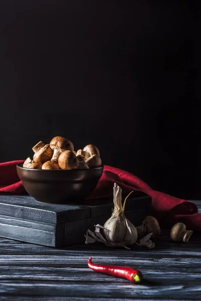 Close up view of bowl with champignons, garlic and chili pepper on wooden table on black — Stock Photo