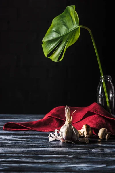 Primer plano vista de ajo, setas y botella con hoja verde en la mesa de madera en negro - foto de stock