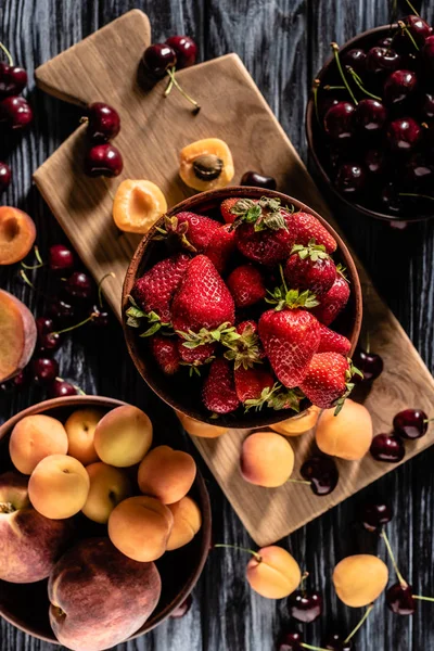 Top view of bowls with cherries, strawberries, peaches and apricots on wooden table — Stock Photo