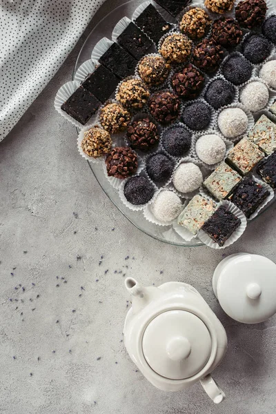 Flat lay with various sweet desserts on plate, teapot and linen on grey surface — Stock Photo