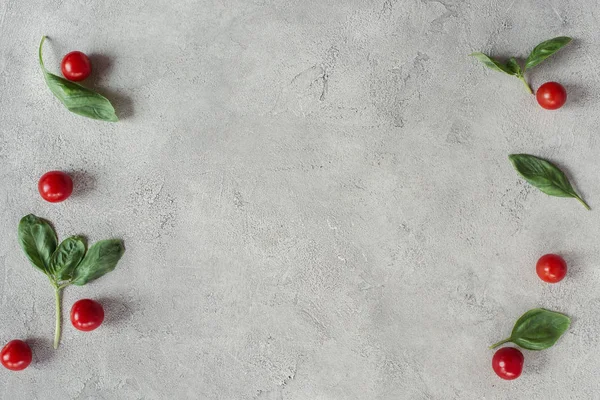 Acostado plano con tomates cherry arreglados y espinacas sobre la mesa gris - foto de stock