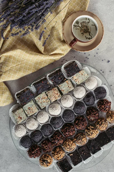 Acostado plano con taza de té de hierbas, postres dulces y lavanda sobre mantel en la mesa gris - foto de stock