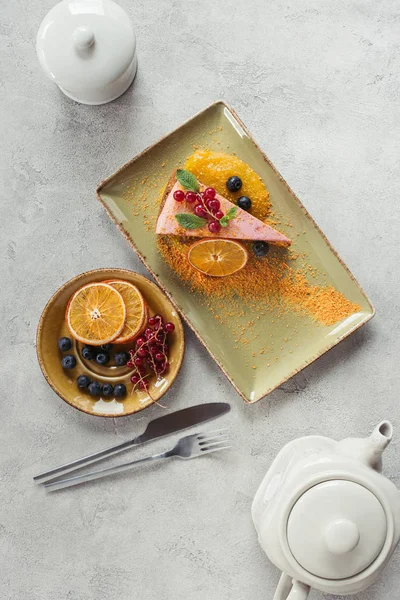 Flat lay with piece of sweet carrot cake with berry filling, teapot and cutlery on grey tabletop — Stock Photo