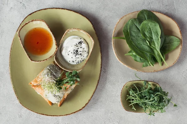 Composizione alimentare con samosa in pasta Phyllo farcita con spinaci e paniera decorata con semi germinati di erba medica e girasole serviti su piatto su superficie grigia — Foto stock