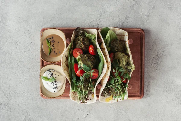 Vue de dessus du falafel aux tortillas, tomates cerises et graines germées de tournesol servies sur planche de bois à la surface grise — Photo de stock