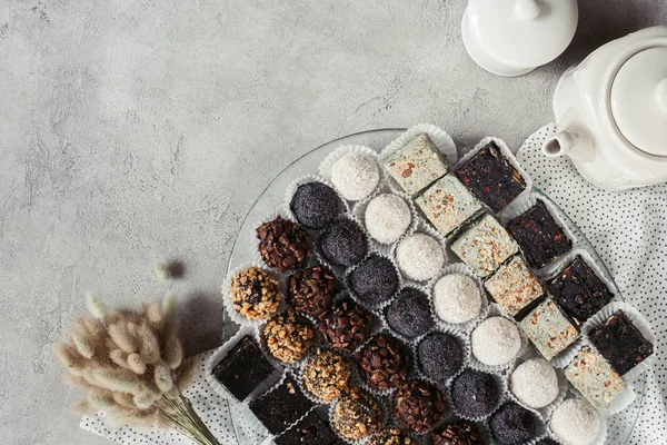 Flat lay with various sweet desserts on plate, teapot and linen on grey surface — Stock Photo