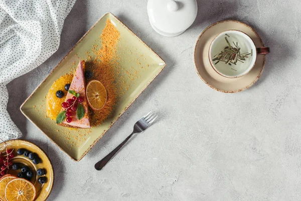 Flat lay with piece of sweet carrot cake with berry filling, cup of herbal tea, linen and fork on grey tabletop — Stock Photo