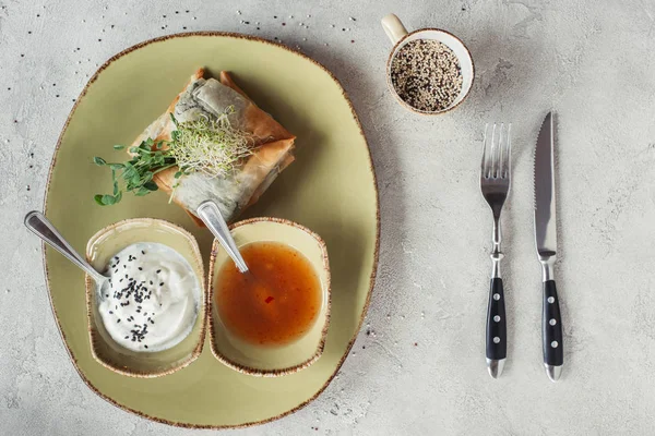 Tendido plano con samosas en Phyllo masa rellena de espinacas y paneer decorado con semillas germinadas de alfalfa y girasol servido en plato sobre mesa gris - foto de stock