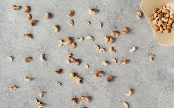 Pose plate avec noix de cajou disposées et bol sur la surface grise — Photo de stock