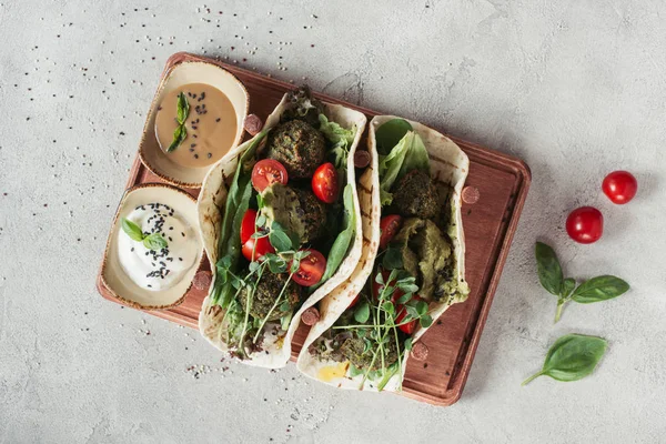 Draufsicht auf Falafel mit Tortillas, Kirschtomaten und gekeimten Sonnenblumenkernen, serviert auf Holzbrett auf grauer Oberfläche — Stockfoto