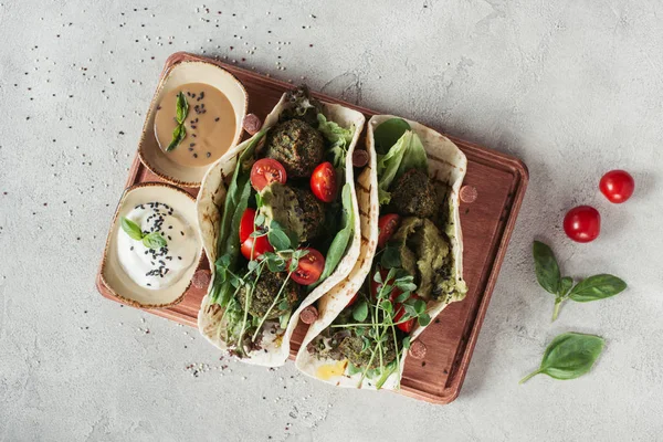 Vue de dessus du falafel aux tortillas, tomates cerises et graines germées de tournesol servies sur planche de bois à la surface grise — Photo de stock