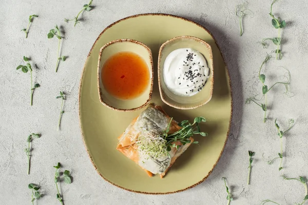 Vista superior de samosas en masa de filo rellenas de espinacas y paneer decoradas con semillas germinadas de alfalfa y girasol servidas en plato sobre superficie gris - foto de stock