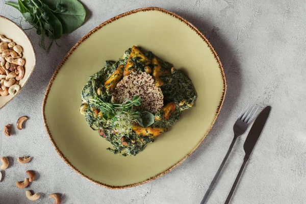 Draufsicht auf Panikesch mit Cashewnüssen und Spinat auf grauer Tischplatte — Stockfoto