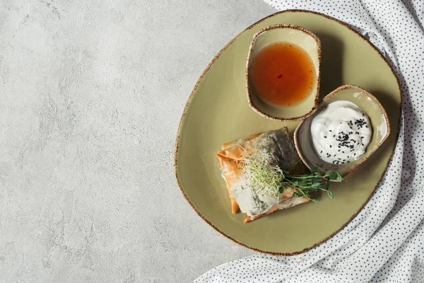 Vista superior de samosas en masa de filo rellenas de espinacas y paneer decoradas con semillas germinadas de alfalfa y girasol servidas en plato sobre superficie gris - foto de stock