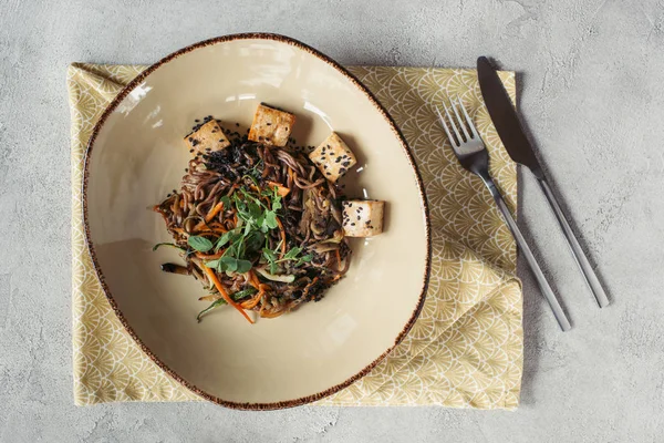 Composición de alimentos con soba con tofu y verduras decoradas con semillas germinadas de girasol sobre una mesa gris - foto de stock