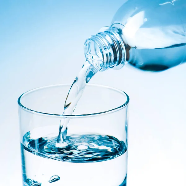Primer plano de verter agua de la botella de plástico en vidrio, tonificado en azul - foto de stock