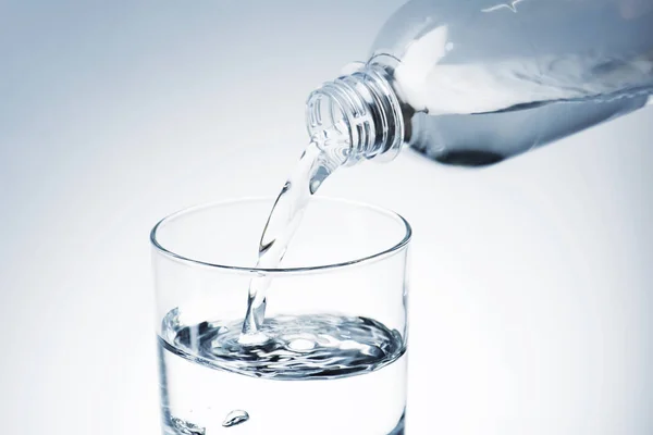 Primo piano colpo di versare l'acqua dalla bottiglia di plastica nel vetro — Foto stock