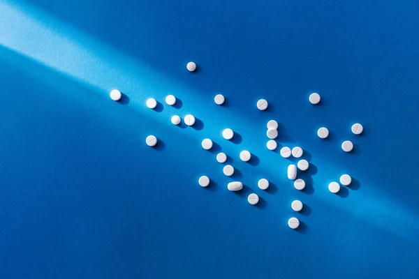 Elevated view of white tablets on blue background with sunlight — Stock Photo