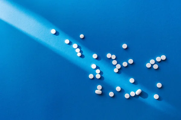 Top view of white pills on blue background with sunlight — Stock Photo