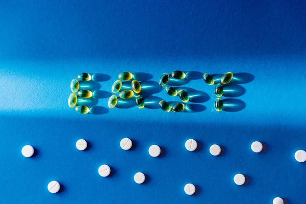 Vista superior de las letras fácil por pastillas cerca de comprimidos blancos sobre fondo azul con luz solar - foto de stock