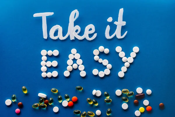 Vista dall'alto di lettering prendere facilmente fatto da pillole bianche vicino a varie compresse su sfondo blu — Foto stock