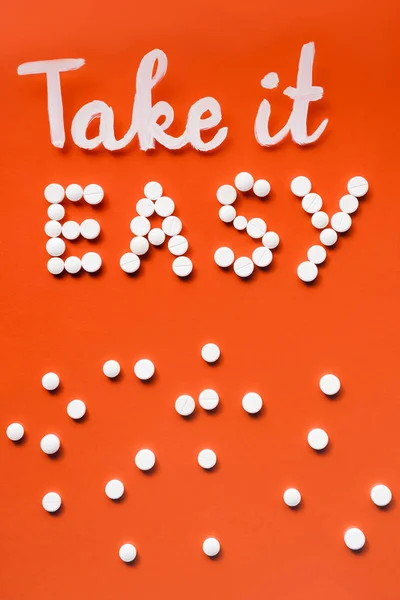 Vista superior de letras ter mais fácil por pílulas brancas no fundo vermelho — Fotografia de Stock
