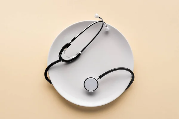 Top view of plate wrapped by stethoscope on beige background — Stock Photo
