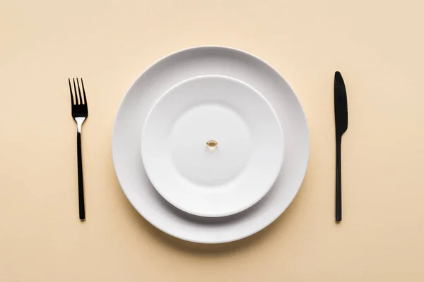 Top view of black fork, knife and plate with one pill on beige background — Stock Photo