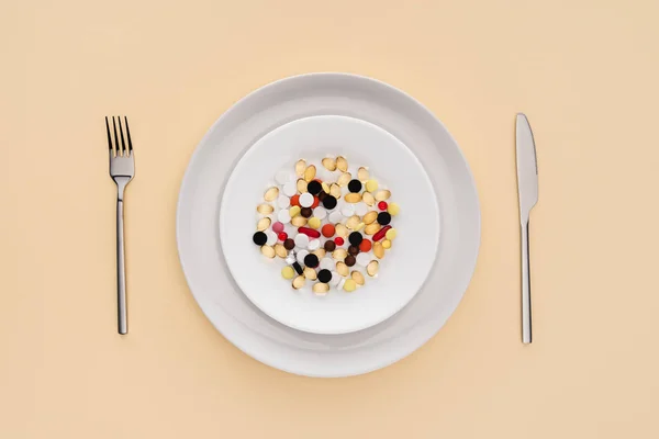 Elevated view of fork, knife and plate with various pills on beige background — Stock Photo