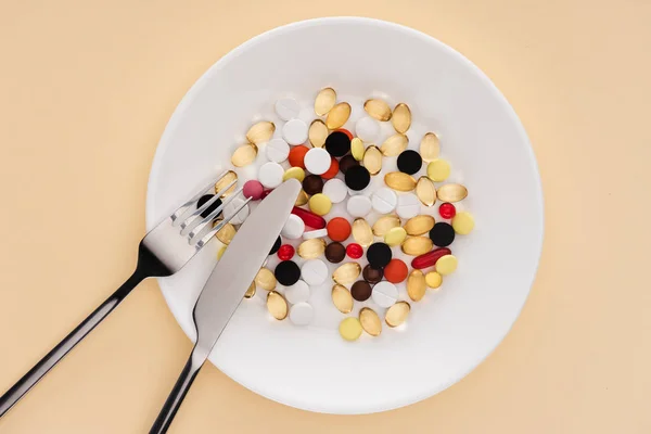 Top view of fork, knife and plate with various pills on beige background — Stock Photo