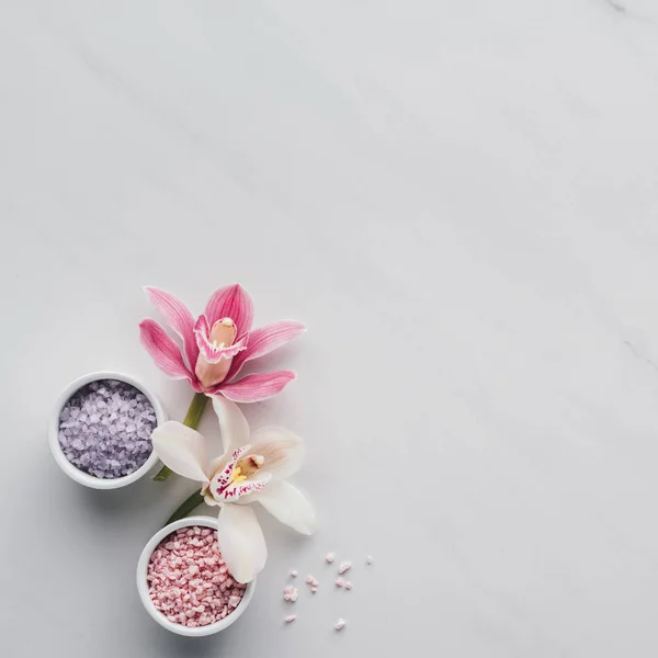 Vista dall'alto di bellissimi fiori di orchidea e sale marino in ciotole su sfondo bianco — Foto stock