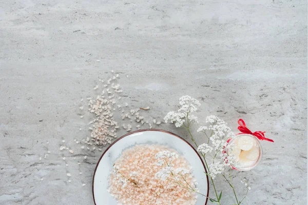 Top view of sea salt in bowl and beautiful small white flowers on grey background — Stock Photo