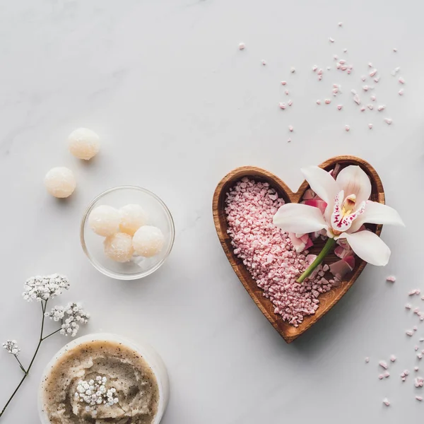 Сверху вид на белый цветок орхидеи и розовая морская соль в форме сердца миска на белом — стоковое фото