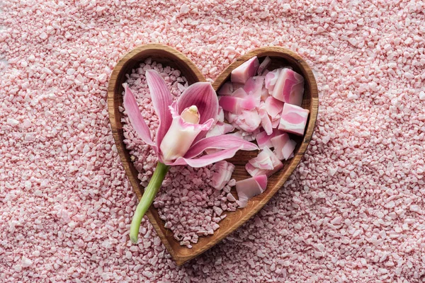 Vista superior de la flor rosada de la orquídea, tazón en forma de corazón, jabón hecho a mano y sal marina - foto de stock