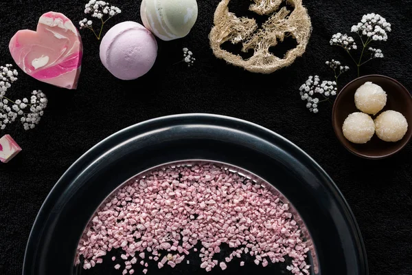 Top view of pink sea salt, handmade soaps and sponge on black — Stock Photo