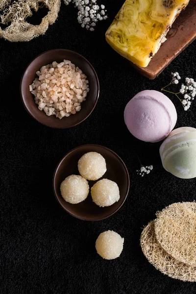 Top view of handmade soaps, sea salt and small white flowers on black sponges — Stock Photo