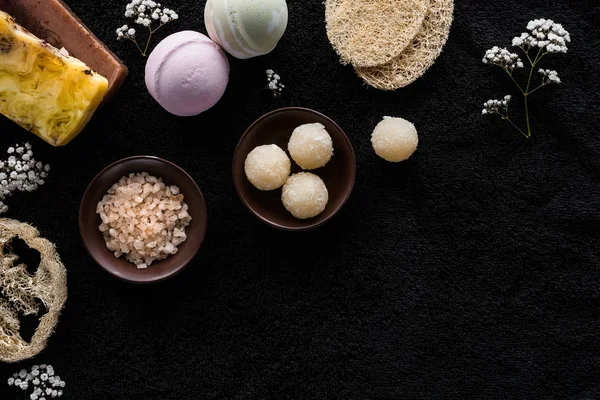 Vue de dessus du gommage fait à la main, sel de mer et petites fleurs blanches sur fond noir — Photo de stock