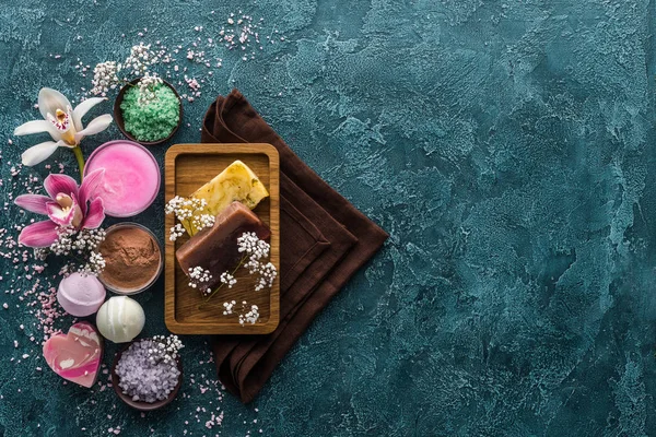 Vue de dessus des savons faits à la main, fleurs, sel de mer et serviettes sur fond sombre — Photo de stock