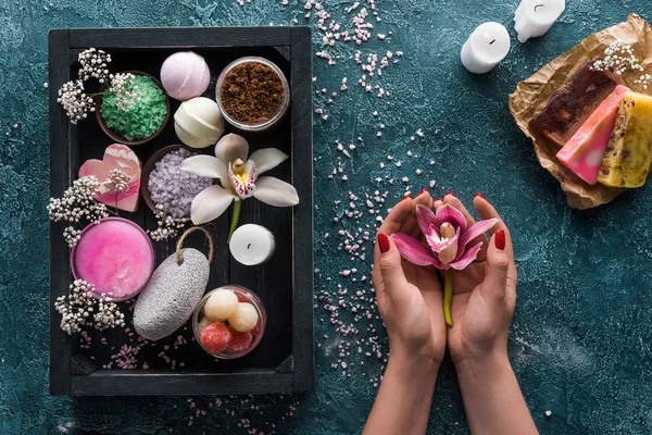 Tiro recortado de la persona que sostiene la flor de la orquídea y los accesorios orgánicos del balneario en caja - foto de stock