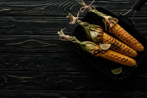 Draufsicht auf Grillpfanne mit gegrilltem Mais und Limettenscheiben auf Holztisch — Stockfoto