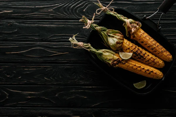 Top view of griddle pan with grilled corn and lime slices on wooden table — Stock Photo